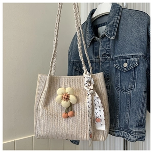 Detail of beige woven tote bag featuring floral charm, cherry pendants and printed silk scarf