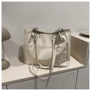 Close-up of beige tote bag with front pockets and silver metal chain strap details
