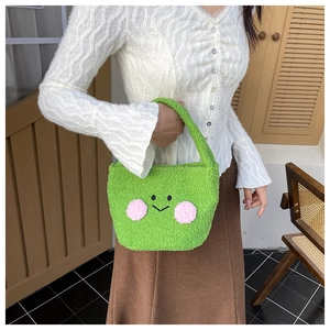 Detailed view of plush green teddy bear handbag with embroidered smiley face on model
