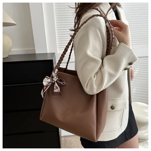 Close-up of brown leather tote bag with woven shoulder strap and vintage floral ribbon scarf