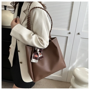 Detail of dark brown tote bag with woven handles and decorative scarf on the strap