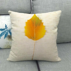 Detail of linen cushion cover featuring a golden autumn leaf print on a grey fabric sofa