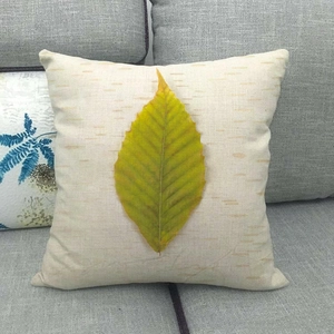 Detail of linen cushion cover with yellow-green autumn leaf print on gray sofa