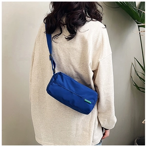 Detail of blue nylon crossbody bag featuring a green label and adjustable shoulder strap