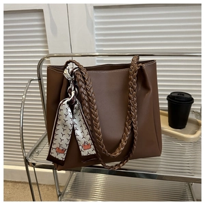 Close-up of brown leather tote bag with woven handle and silk scarf detail on a glass shelf