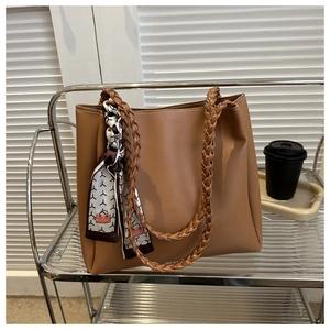 Close-up of brown tote bag featuring woven handles and decorative printed silk scarf detail