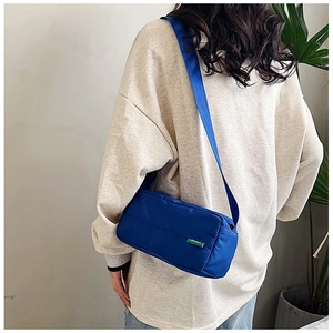 Borsa a tracolla in nylon blu con cinghia e etichetta logo verde su maglione bianco