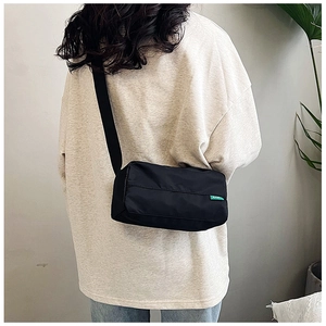 Dettaglio della borsa a cuscino in nylon nero con etichetta logo verde sulla spalla