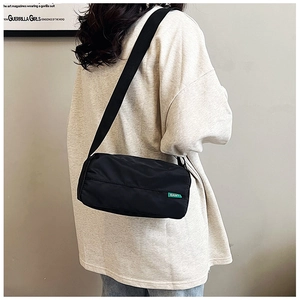 Detailed side view of black nylon cylinder bag with green label and wide shoulder strap