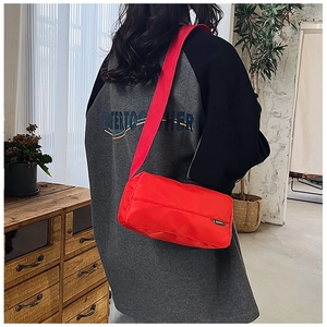 Dettaglio borsa a tracolla in nylon rosso con etichetta verde e ampia tracolla in tessuto