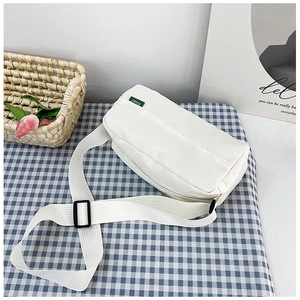 Close-up of white nylon crossbody bag with wide adjustable strap on a plaid cloth