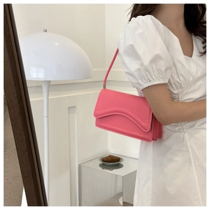 Roze leren schoudertas met unieke golfvormige flap gedragen door een model