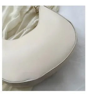 Macro detail of creamy white half-moon underarm bag with gold printed fashion logo text