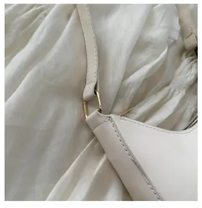 Detailed close-up of light beige leather shoulder bag with gold-tone buckle and stitching