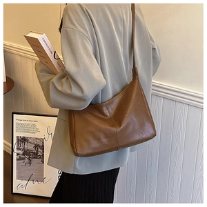 Detail view of dark brown leather tote bag with glossy texture worn on shoulder
