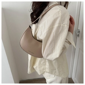 Minimalist beige crescent underarm bag shown in a lifestyle setting on a striped shirt