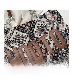 Detail of woven tote bag showing geometric patterns, leather patch, and metal chain strap