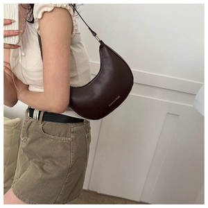 Detail of a dark brown crescent-shaped shoulder bag with gold lettering and leather strap