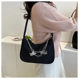 Détail du sac sous le bras en toile noire avec chaînes argentées et breloques papillon