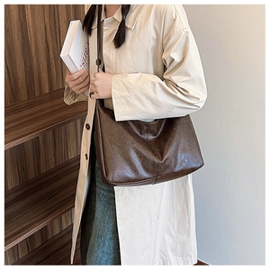 Detail of vintage brown leather tote bag with oily texture on a trench coat model