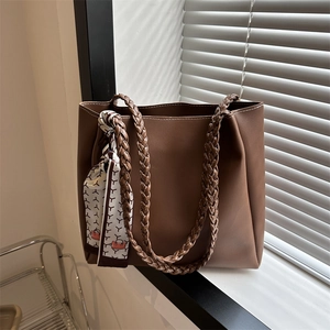 Brown leather tote bag with woven handles and floral scarf detail in natural window light