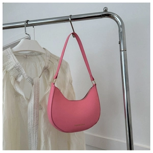 Detail of rose pink crescent shoulder bag with gold lettering on a white shirt background