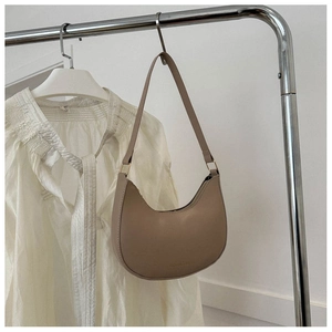 Detail of khaki leather shoulder bag hanging on stand with gold buckle and printed text