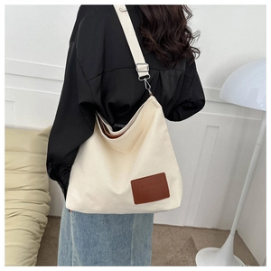 Detalle de bolso tote de lona beige con parche de cuero y correa ancha ajustable