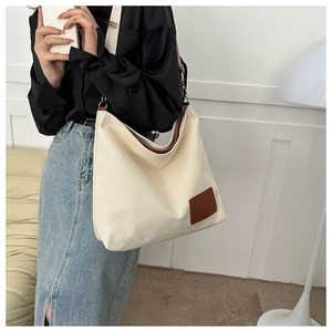 Detalle de bolso tote de lona blanca con parche de logo de cuero marrón y bandolera