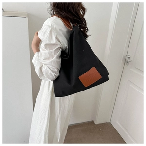 Detalle de bolso tote de lona negra con correas de cuero marrón y etiqueta de moda