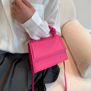 Vibrant rose pink knotted handbag with crossbody strap shown in a minimalist setting