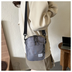 Détail d'un sac bandoulière en nylon gris avec étiquette HELLO WEEKEND et zips à nœuds décoratifs