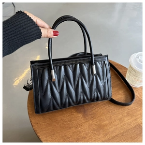 Detail of black wave quilted crossbody bag showing texture and leather hand strap