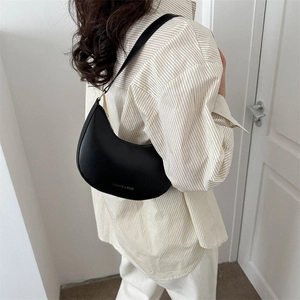 Minimalist black crescent shoulder bag in matte faux leather worn by a model
