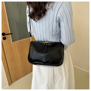 Detail of minimalist black leather tote bag featuring gold hardware and zipper