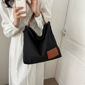 Bolso tote de lona negra minimalista con asas de cuero marrón y hebilla de metal