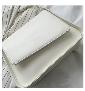 Close-up of white leather square crossbody bag with fine stitching on fabric texture