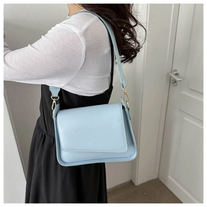 Close-up of light blue leather shoulder bag featuring an asymmetric flap and gold metal hooks