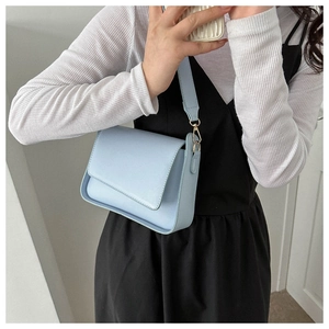 Detail of light blue trapezoid shoulder bag with wide strap and gold hardware accents