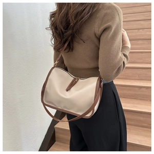 Detail of a minimalist beige crossbody bag with brown leather trim and metallic zipper