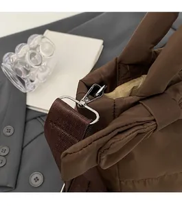 Detail of coffee brown quilted nylon bag with silver swivel hook and woven strap