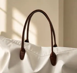 Primer plano del bolso tote blanco con asas de cuero marrón reforzadas y cremallera