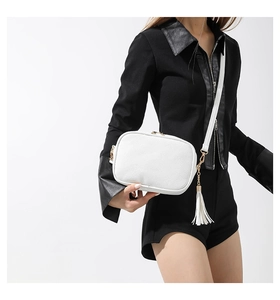 Close-up of white pebble leather crossbody bag featuring gold hardware and tassel detail