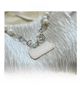 Detail of white pleated handbag featuring pearl strap and flower metal buckle with fashion tag