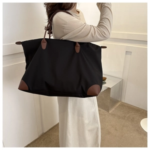 Detalle de bolsa de viaje de nailon negro con asas de cuero marrón llevada al hombro