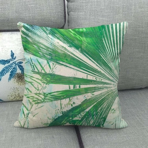 Minimalist linen pillowcase with green palm leaf print on a grey sofa in home setting