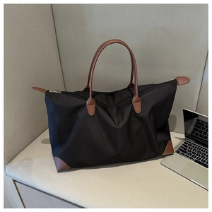Detalle de bolsa de viaje de nailon negro con asas de cuero marrón y cremallera dorada