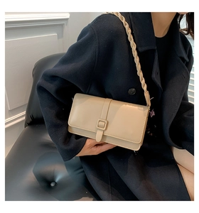 Dettaglio borsa a tracolla beige chiaro con spallina intrecciata su cappotto scuro