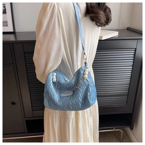 Blue pleated cloud bag with elegant pearl and metal chain detail on model shoulder
