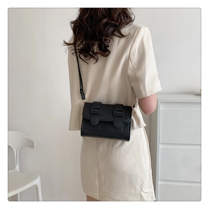 Minimalist black rectangular crossbody bag styled on shoulder in a modern setting